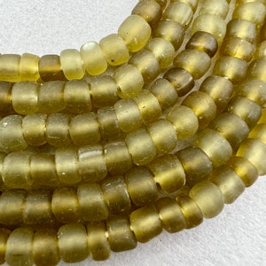 Peut inclure: Gros plan sur un brin de perles en verre vert olive. Les perles sont rondes et ont une finition légèrement givrée.