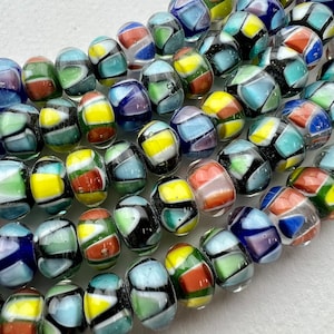 May include: A strand of colorful glass beads with a variety of geometric patterns. The beads are clear with black, white, yellow, red, blue, and green accents.