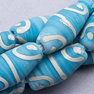 May include: A close-up of a string of turquoise blue and white ceramic beads. The beads are cylindrical and have a swirling pattern.