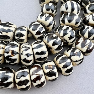 May include: A close-up of a strand of black and white patterned beads. The beads are made of bone or wood and have a natural, rustic look.