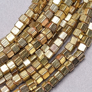 May include: A strand of gold-toned metal beads, each bead is a faceted cube with a slightly irregular shape.