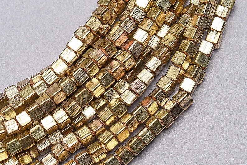 May include: A strand of gold-toned metal beads, each bead is a faceted cube with a slightly irregular shape.