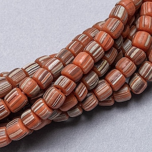 May include: A close-up of a strand of orange and white striped glass beads. The beads are cylindrical and have a smooth, polished finish.