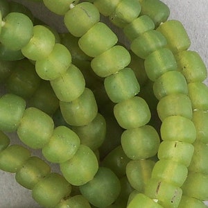 May include: Close-up of a strand of light green glass beads. The beads are round and have a slightly irregular shape. They are strung together on a clear thread.