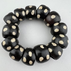 May include: A black and white beaded bracelet with white polka dots on each bead. The bracelet is made of round beads and is approximately 10 inches in circumference.