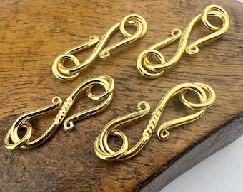 May include: Four gold-toned metal clasps with a decorative swirl design. The clasps are arranged in a staggered pattern on a wooden surface.