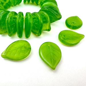 May include: Bright green glass leaf beads and a strand of matching beads. The beads have a translucent quality, with visible leaf vein details. The beads are suitable for jewelry making and other craft projects.