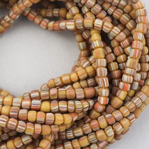 May include: A close-up of a strand of multi-colored glass beads. The beads are small and round, with a variety of colors, including yellow, orange, brown, and white. The beads are arranged in a circular pattern, creating a visually appealing design.