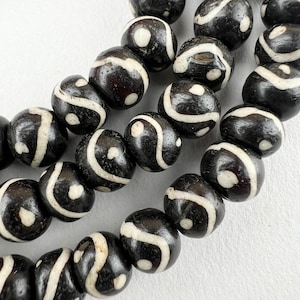Peut inclure: Un collier de perles noires et blanches avec un motif en spirale. Les perles sont en matériau lisse et poli.