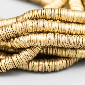 Pu&ograve; includere: Primo piano di una collana di perline di metallo dorato. Le perline sono rotonde e hanno una superficie testurizzata.