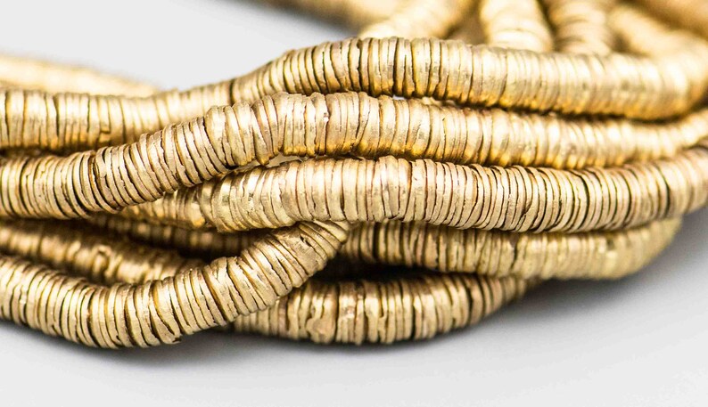 Pu&ograve; includere: Primo piano di una collana di perline di metallo dorato. Le perline sono rotonde e hanno una superficie testurizzata.