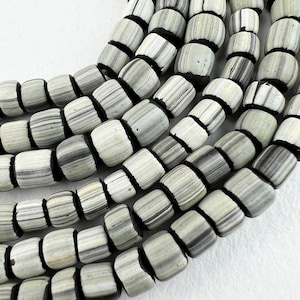 May include: A close-up of a strand of white and gray striped glass beads with black trim. The beads are cylindrical and have a slightly irregular shape.