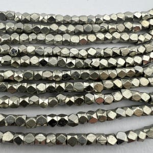 May include: A strand of silver-toned metal beads, each bead is faceted and has a hexagonal shape.