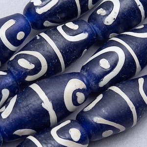 Puede incluir: Primer plano de una hilera de cuentas de vidrio azul y blanco. Las cuentas son cilíndricas y tienen un patrón de pintura blanca en espiral sobre un fondo azul oscuro.