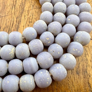 May include: A strand of light purple glass beads with a speckled white finish. The beads are round and have a slightly irregular shape.