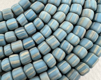 May include: A close-up of a strand of light blue glass beads with white stripes. The beads are cylindrical and have a slightly irregular shape.