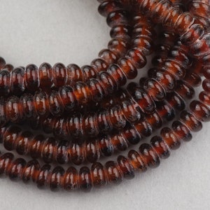 May include: A strand of brown glass beads with a spiral design. The beads are translucent and have a slightly iridescent finish.