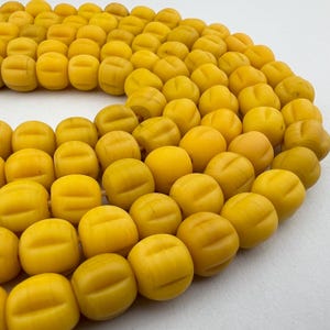 May include: A strand of yellow, round beads with a textured surface. The beads are strung together to form a necklace or bracelet.