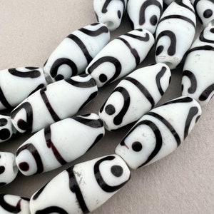 Peut inclure: Un ensemble de perles en verre blanches et noires avec un motif en spirale. Les perles sont de forme ovale et ont une finition brillante.