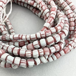 May include: Strands of white and red striped beads. The beads are cylindrical with rounded edges and a pattern of alternating white and red stripes. The beads are strung together, creating a necklace or bracelet.