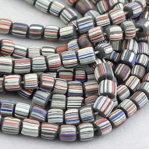 May include: A strand of colorful glass beads with a striped pattern in shades of white, black, red, and blue. The beads are cylindrical and have a slightly rounded shape.