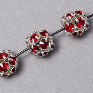 May include: Three red rhinestone beads strung on a silver wire. The beads are round and have a silver metal frame.