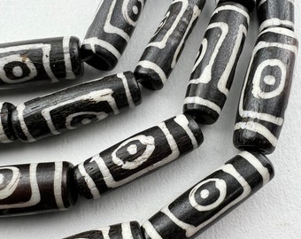 May include: A close-up of a strand of black and white cylindrical beads with a geometric pattern. The beads are made of agate and have a smooth, polished finish.
