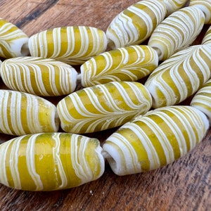 May include: A close-up of a string of yellow and white glass beads. The beads are oval shaped and have a swirling pattern.