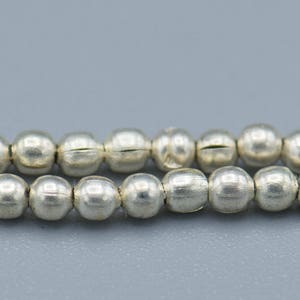 以下が含まれることがあります： 銀色のビーズのストランド。各ビーズは丸く、わずかにテクスチャ加工された表面をしています。