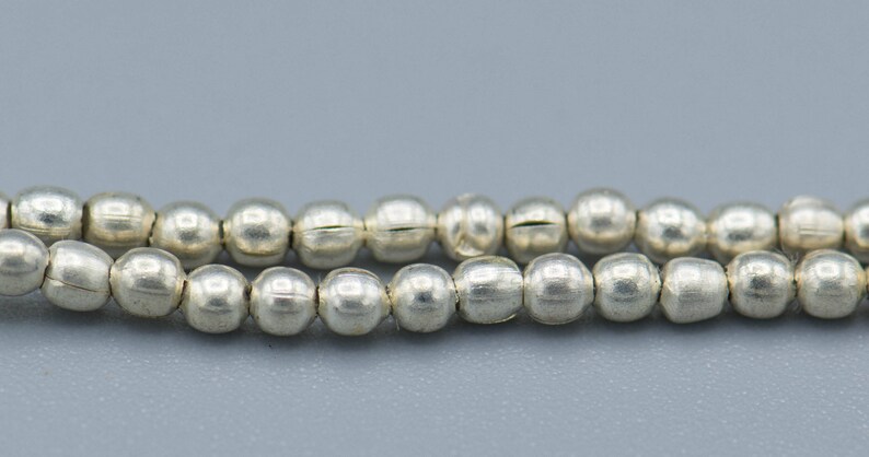 以下が含まれることがあります： 銀色のビーズのストランド。各ビーズは丸く、わずかにテクスチャ加工された表面をしています。