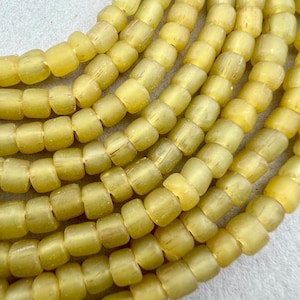May include: A strand of pale yellow glass beads. The beads are small and round, with a slightly frosted finish.