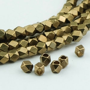 May include: A strand of gold-toned metal beads with a faceted, geometric shape. The beads are strung together to form a necklace or bracelet. There are also several loose beads in the image.