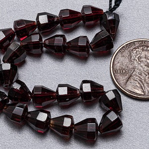 May include: A strand of dark red faceted glass beads, approximately the size of a US penny.