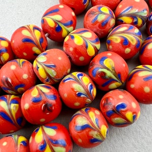 May include: A collection of red glass beads with yellow, blue and white swirl patterns. The beads are round and have a glossy finish.