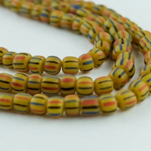 May include: Strands of yellow beads with horizontal stripes in red, blue, and black. The beads are round and appear to be made of glass or a similar material. The beads are strung together, creating a necklace or bracelet.