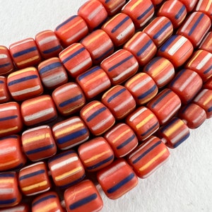 May include: A strand of colorful glass beads with a striped pattern in shades of orange, white, and blue. The beads are cylindrical and have a slightly rounded shape.