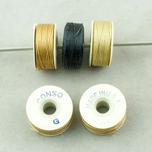 May include: Three spools of thread on a white plastic bobbin. The thread colors are beige, black, and tan. The bobbins have the text "CONSO" and "MADE IN USA" printed on them.