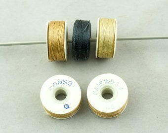 May include: Three spools of thread on a white plastic bobbin. The thread colors are beige, black, and tan. The bobbins have the text "CONSO" and "MADE IN USA" printed on them.