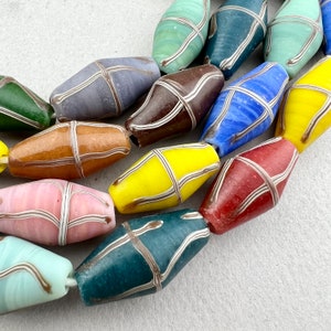 Puede incluir: Una colección de cuentas de vidrio de colores con rayas blancas. Las cuentas son de diferentes formas y tamaños, y están enhebradas en una cuerda.