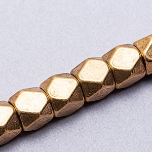 May include: A strand of gold-toned metal beads, each bead is a hexagonal shape with a faceted surface.