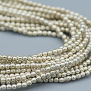 以下が含まれることがあります： 滑らかで光沢のある仕上げの銀色のビーズの糸。ビーズは小さく丸く、長い連続した糸に糸でつながれています。