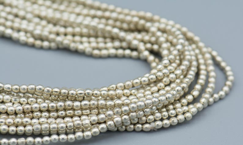 以下が含まれることがあります： 滑らかで光沢のある仕上げの銀色のビーズの糸。ビーズは小さく丸く、長い連続した糸に糸でつながれています。