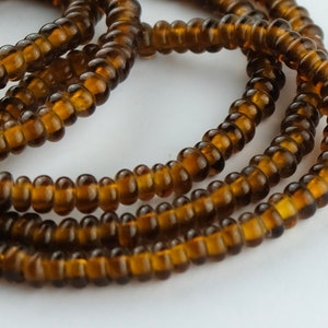 May include: A strand of brown glass seed beads. The beads are small and round, and they are strung together on a clear thread.