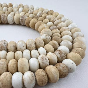 May include: A strand of off-white and cream-coloured glass beads with a speckled texture. The beads are round and have a slightly irregular shape.