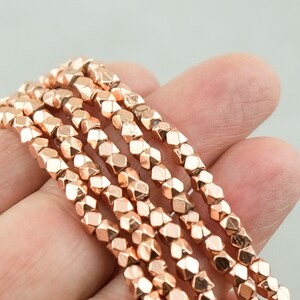 May include: A strand of rose gold faceted beads. The beads are small and have a geometric shape.