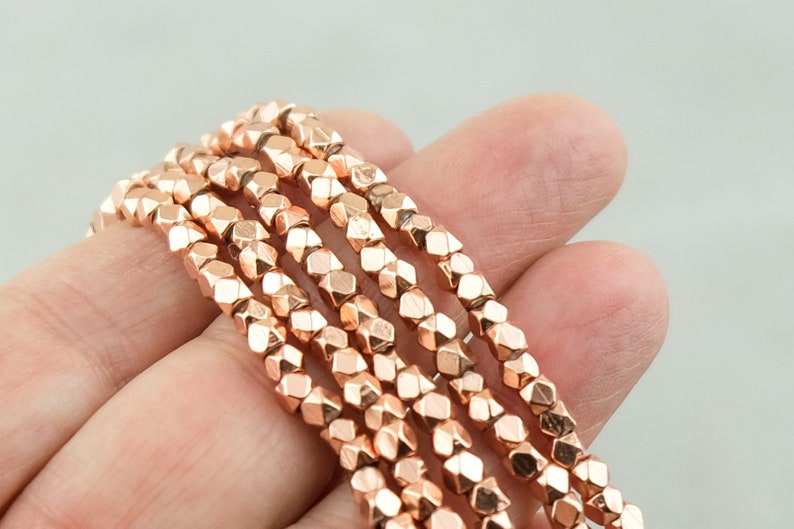 May include: A strand of rose gold faceted beads. The beads are small and have a geometric shape.
