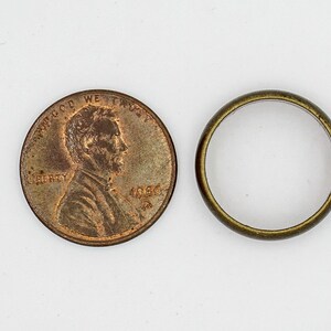 Pu&ograve; includere: Una moneta da un centesimo americana di colore rame con l'immagine di Abraham Lincoln e il testo "IN GOD WE TRUST" e "LIBERTY" su un lato e l'anno "1966" sull'altro. Accanto alla moneta c'&egrave; un anello di metallo dorato.
