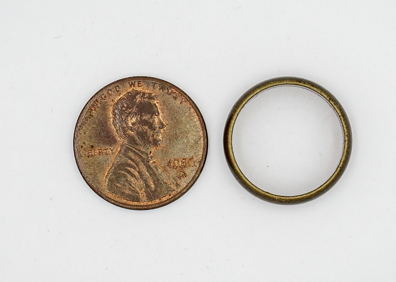 Pu&ograve; includere: Una moneta da un centesimo americana di colore rame con l'immagine di Abraham Lincoln e il testo "IN GOD WE TRUST" e "LIBERTY" su un lato e l'anno "1966" sull'altro. Accanto alla moneta c'&egrave; un anello di metallo dorato.