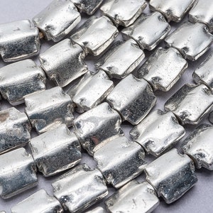 May include: A strand of silver-toned metal beads, each bead is rectangular with a slightly irregular shape. The beads are arranged in a staggered pattern, creating a textured look.