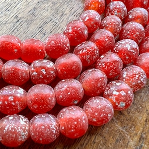 May include: A close-up of a strand of red glass beads with white speckles. The beads are round and have a slightly irregular shape.